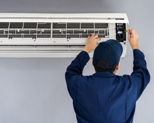 Electrician with screwdriver repairing the air conditioner indoors